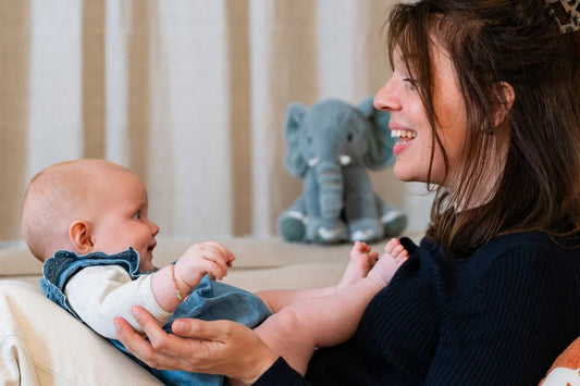 Een moeder en kind genieten samen van een liefdevol moment terwijl op de achtergrond Milody, de gepersonaliseerde muziekknuffel, te zien is. De knuffel speelt een persoonlijk liedje dat zorgt voor verbinding en rust.